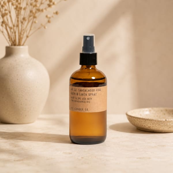 Amber room spray bottle on a neutral tabletop with a ceramic vase and bowl