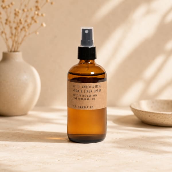 Amber room spray bottle with a black pump on a neutral tabletop