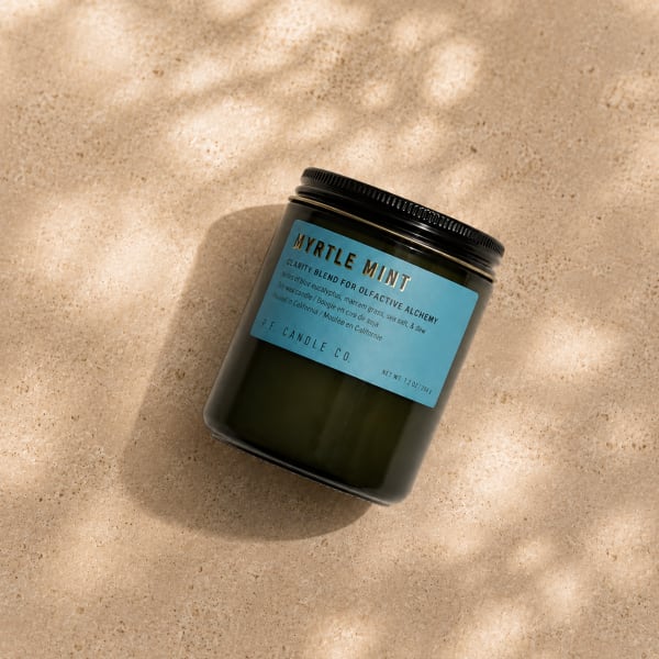 Black jar candle with a blue label on a beige surface