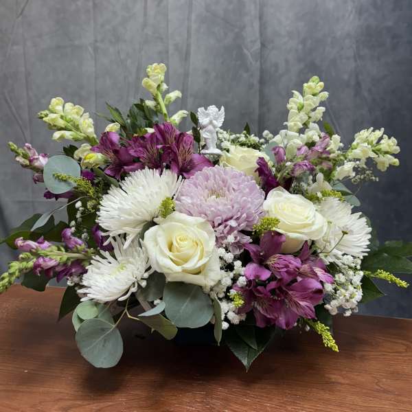 Mixed bouquet of white roses, purple flowers, and white daisies in a low container