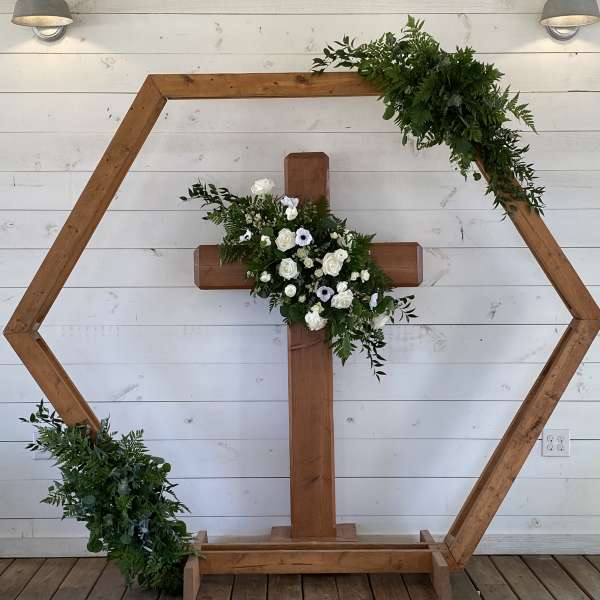 Wooden cross with white flowers and greenery on a hexagonal frame