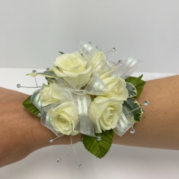 Wrist corsage of ivory roses with iridescent ribbon and crystal bead accents on an arm.