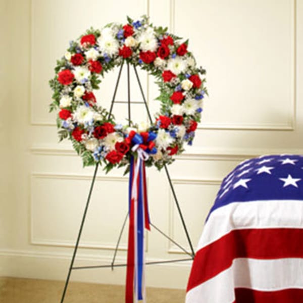 Red, white, and blue floral wreath on a stand with ribbon streamers