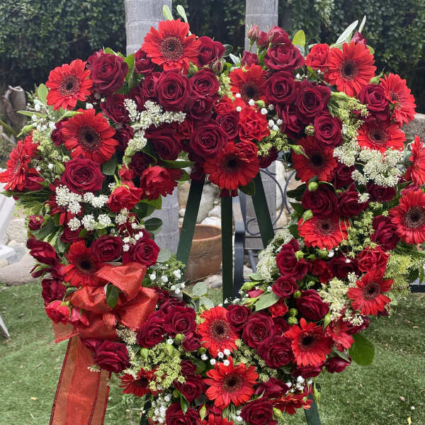 Heart-shaped wreath of red roses and gerbera daisies with a red ribbon