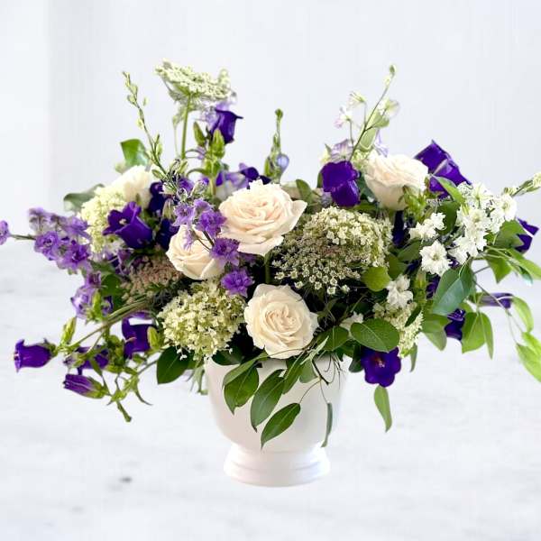 White roses and purple bellflowers arranged in a white vase