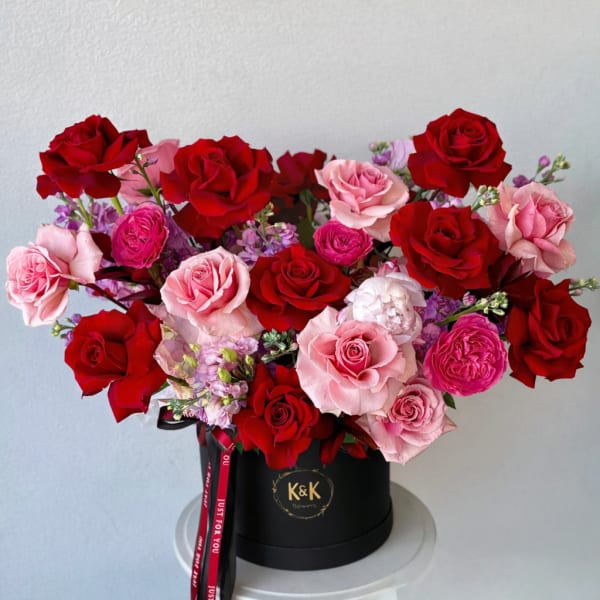 Red and pink roses arranged in a black hat box with a ribbon