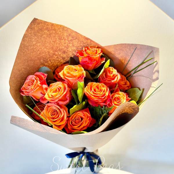 Bouquet of orange and pink roses wrapped in brown paper