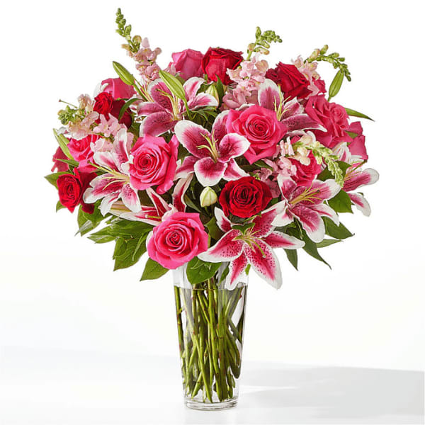 Tall glass vase of hot pink and red roses with pink stargazer lilies and snapdragons.