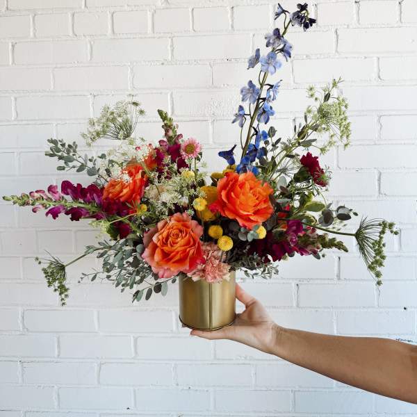 Colorful mixed bouquet in a gold vase with orange, blue, and magenta flowers