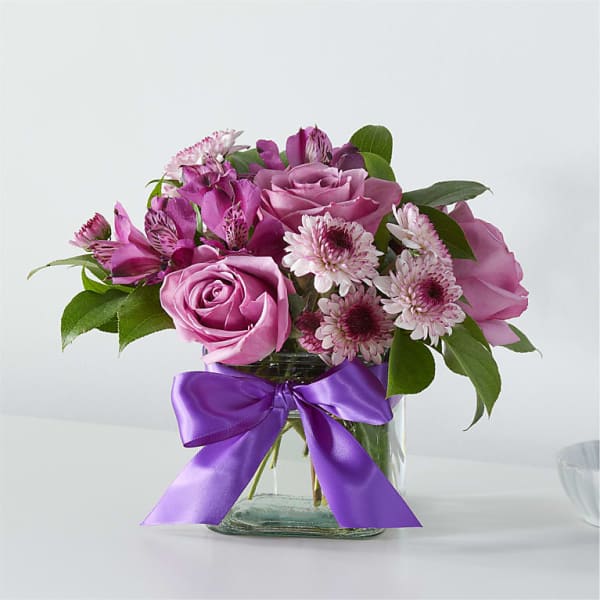 Pink roses and purple flowers in a glass vase with a purple ribbon