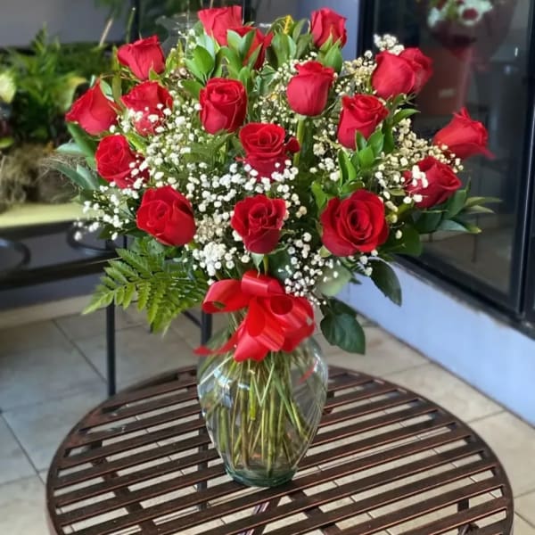 Red roses arranged in a clear glass vase with baby's breath and a red ribbon
