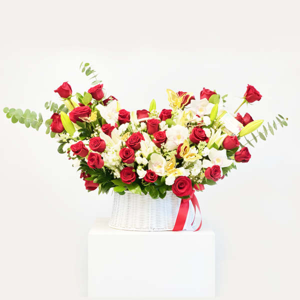 Red roses and white orchids in a white basket with a red ribbon