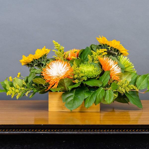 Low floral arrangement with sunflowers and orange-white blooms in a wooden box