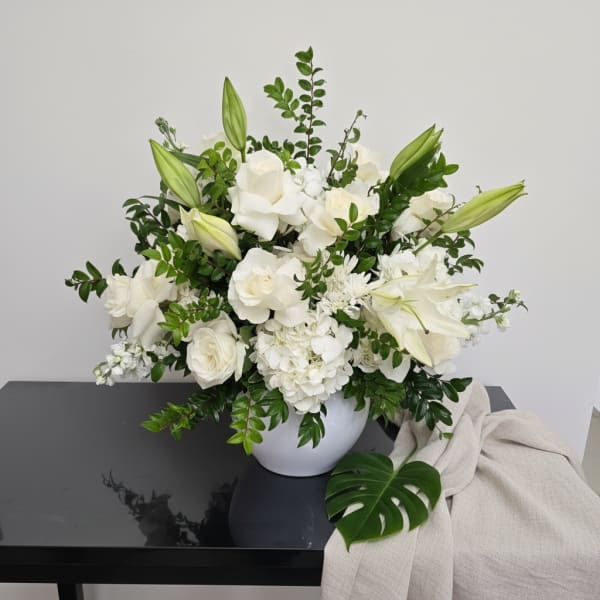 White floral arrangement in a round vase with lilies and roses