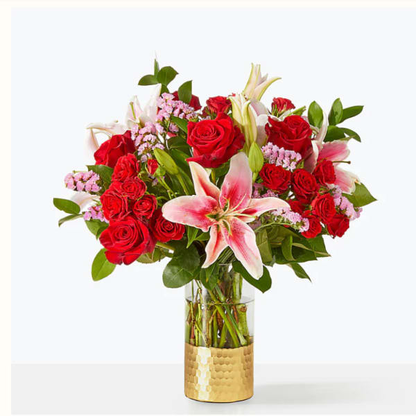 Red roses and pink lilies in a glass vase with a gold base