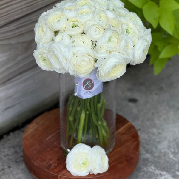 White ranunculus bouquet in a clear glass vase on a wooden stand