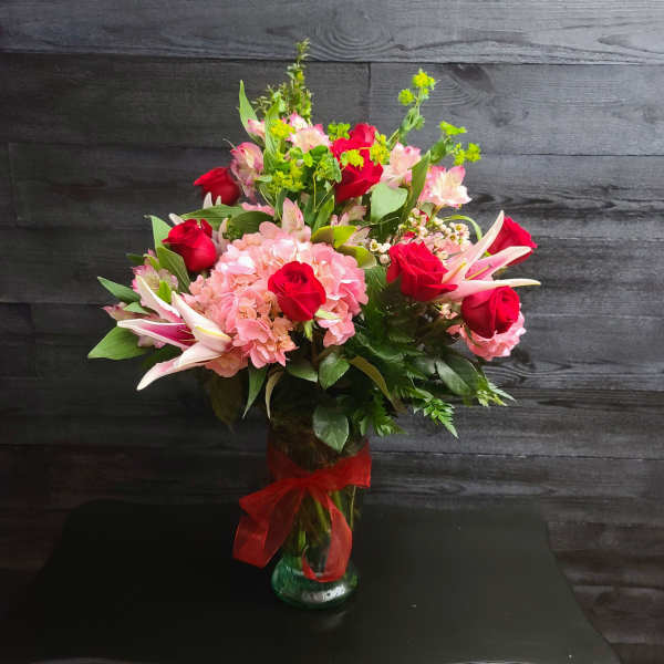 Bouquet of red roses, pink hydrangeas, and lilies in a glass vase