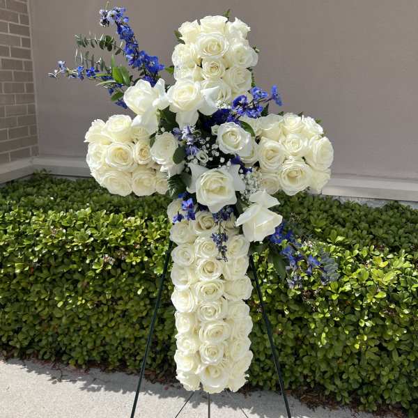 White rose cross-shaped floral tribute with blue accents on an easel