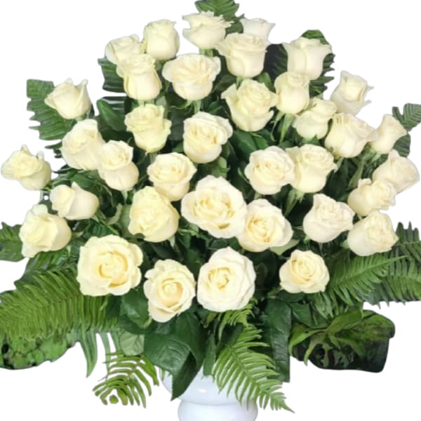 White rose arrangement in a white vase with broad fern foliage