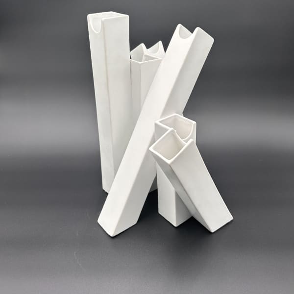 Four white ceramic vases with angular openings on a dark background
