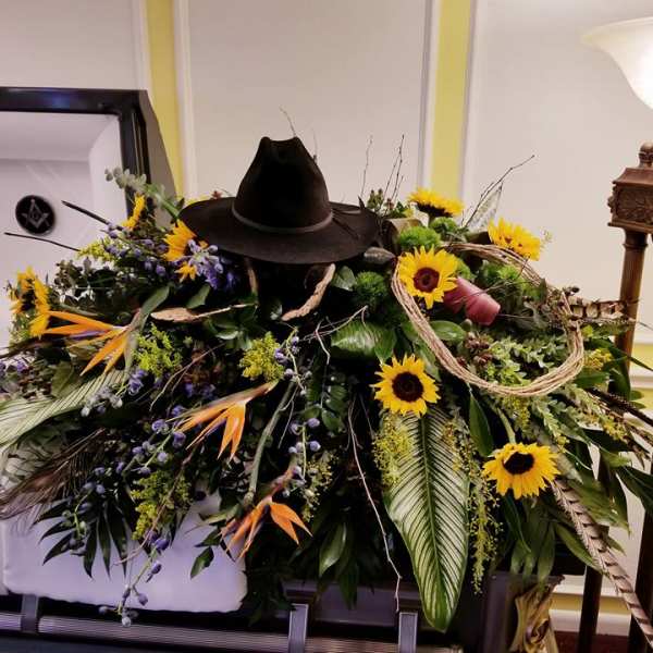 Large funeral casket spray with sunflowers and a black cowboy hat