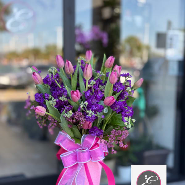 Pink tulips and purple flowers in a wrapped bouquet with a ribbon