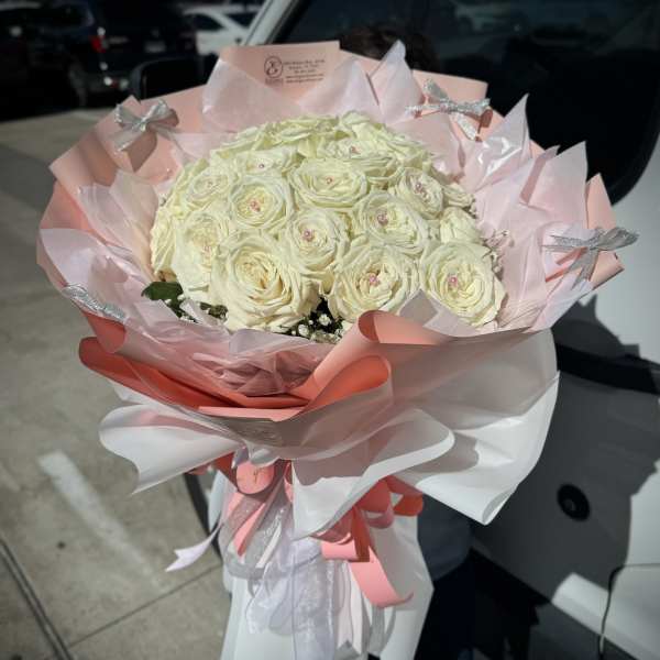 Bouquet of white roses wrapped in pink and white paper with silver bows