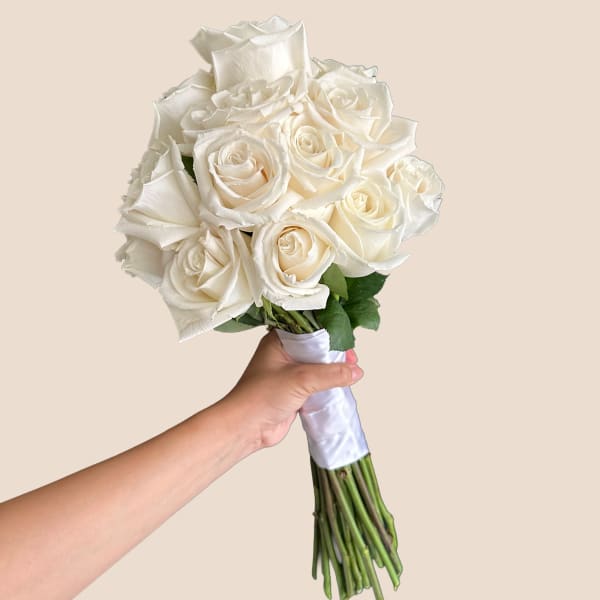Handheld bouquet of white roses wrapped in white ribbon