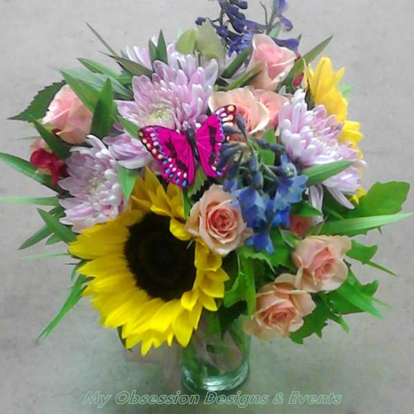 Mixed bouquet with sunflowers, roses, and purple blooms in a glass vase