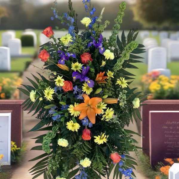 Tall funeral spray with orange, yellow, purple, and blue flowers