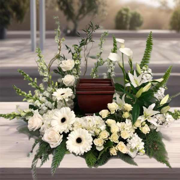 White floral funeral arrangement surrounding a wooden urn