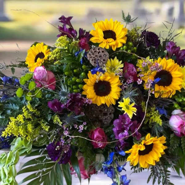 Colorful floral casket spray with sunflowers, roses, and purple blooms