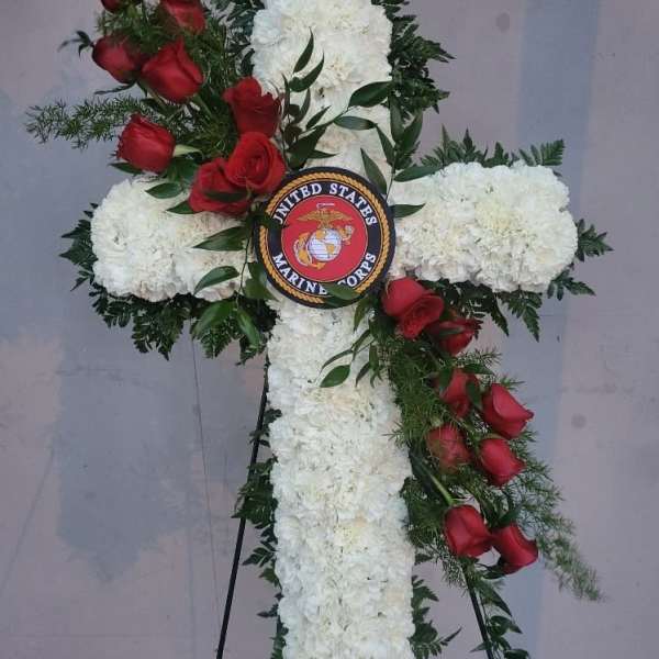 Cross-shaped floral tribute with white blooms and red roses on an easel