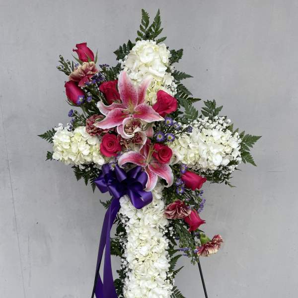Cross-shaped floral funeral spray with white hydrangeas, pink lilies, and roses
