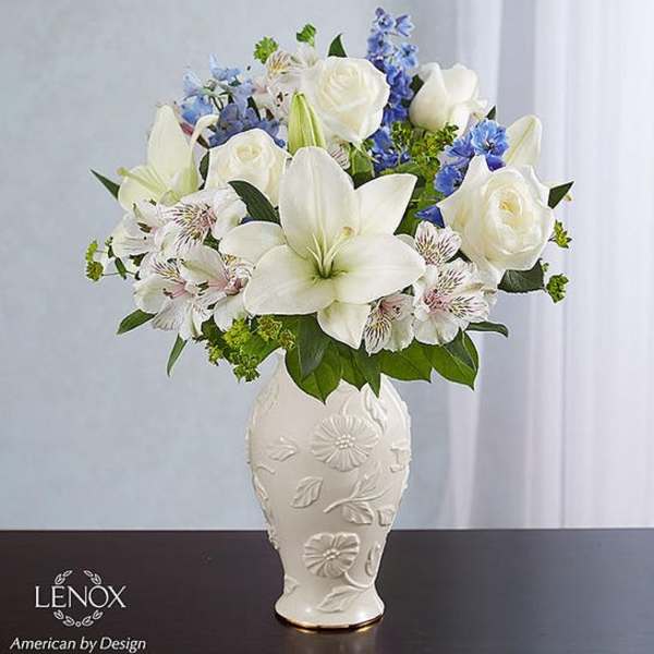 White lilies and roses arranged in a decorative vase with blue accents