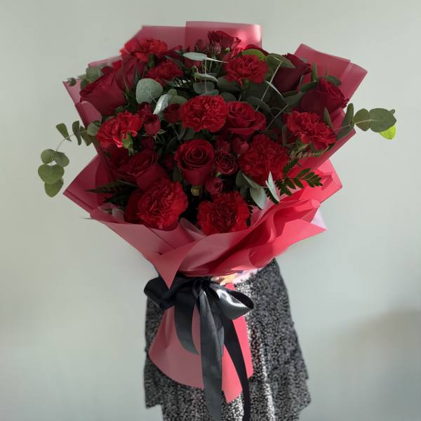 Bouquet of red roses and carnations wrapped in pink paper with a black ribbon