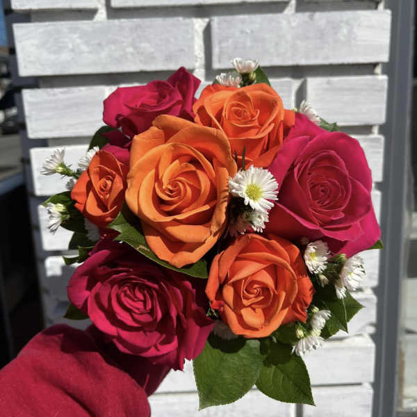 Handheld bouquet of orange and pink roses with small white daisies