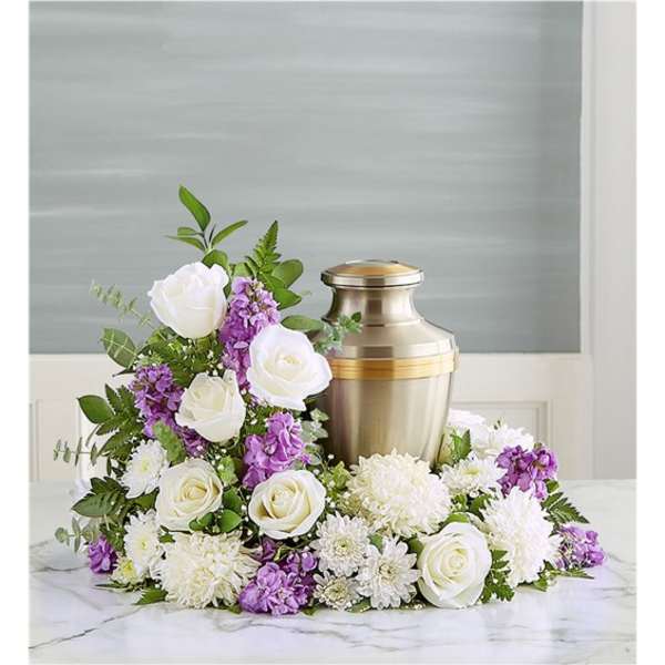 Cremation urn surrounded by white roses, white mums, and purple flowers in a crescent arrangement