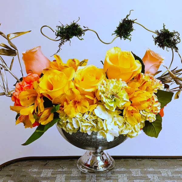 Yellow and orange flower arrangement in a silver pedestal vase