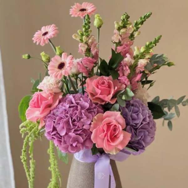 Pink and purple bouquet in a textured vase with a lavender ribbon