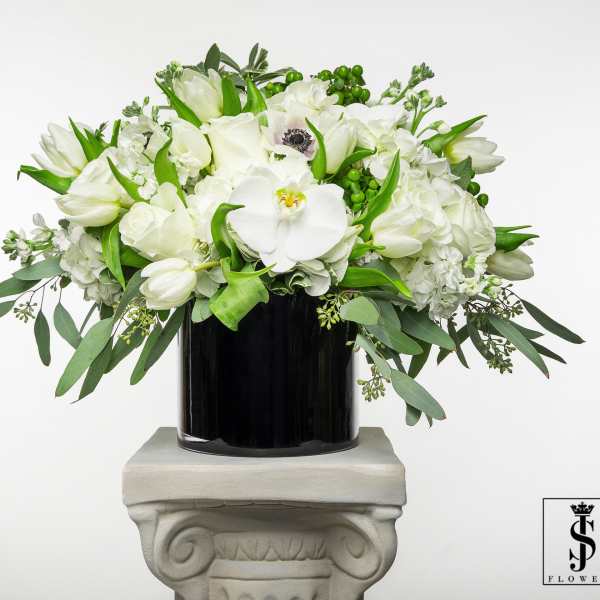 White floral arrangement in a black vase with trailing greenery