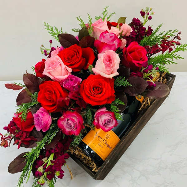 Red and pink roses arranged in a gift box with a champagne bottle