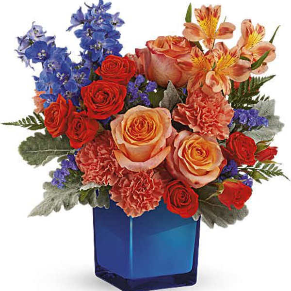 Mixed bouquet of roses, carnations, and blue flowers in a blue glass vase