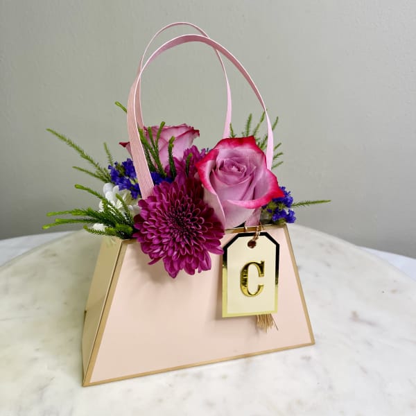 Pink rose and purple chrysanthemum arrangement in a gift bag with a letter tag
