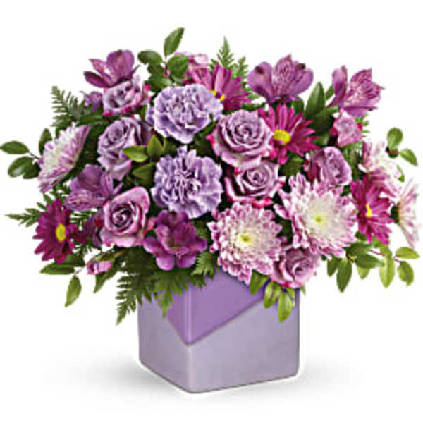 Purple mixed flower arrangement in a lavender square vase