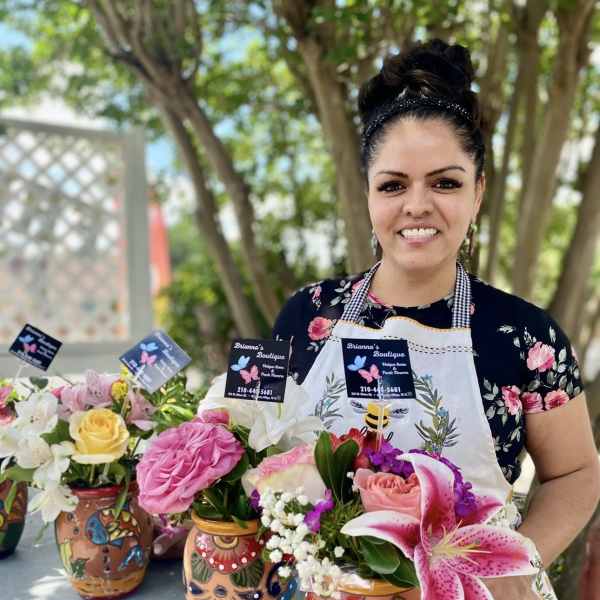Woman holding colorful flower arrangements in painted ceramic vases outdoors.
