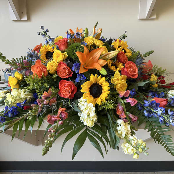 Large colorful floral casket spray with roses, sunflowers, lilies, and orchids