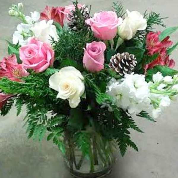 Pink and white roses arranged in a glass vase with greenery and a pinecone