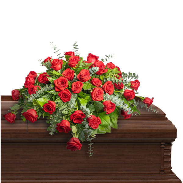 Red rose casket spray with greenery on a wooden casket