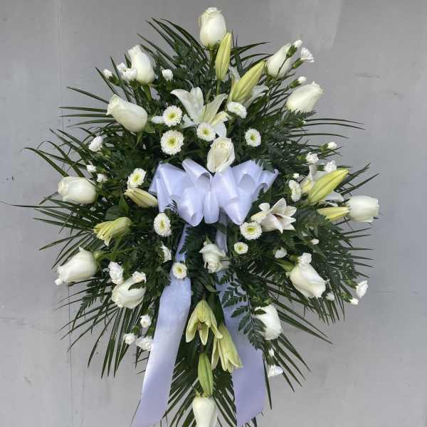 White floral standing spray with lilies and roses on a ribboned easel